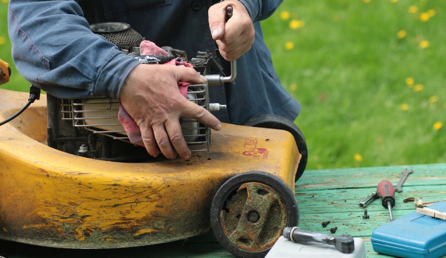 A man working on a non-functional lawn mower, attempting to resolve start-up problems.